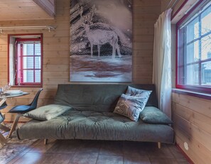A cozy room with a wooden interior, a sofa with cushions, a dining table with chairs, and a painting of a snowy landscape on the wall. - Levin Otava - Comfy Apt in Levi Centre (Kittilä)