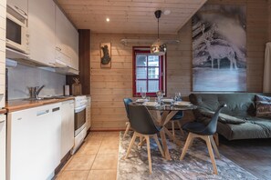 A modern kitchen with white cabinetry, a built-in oven, and a dining area with a glass table and chairs. - Levin Otava - Comfy Apt in Levi Centre (Kittilä)