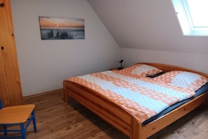 Une chambre avec un plafond en pente, un lit avec une literie à motifs, une chaise en bois et un tableau accroché au mur.