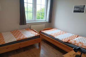 Ein Zimmer mit zwei hölzernen Betten, einem fenster mit Vorhängen, einem Heizkörper und einem gerahmten Bild an der Wand.