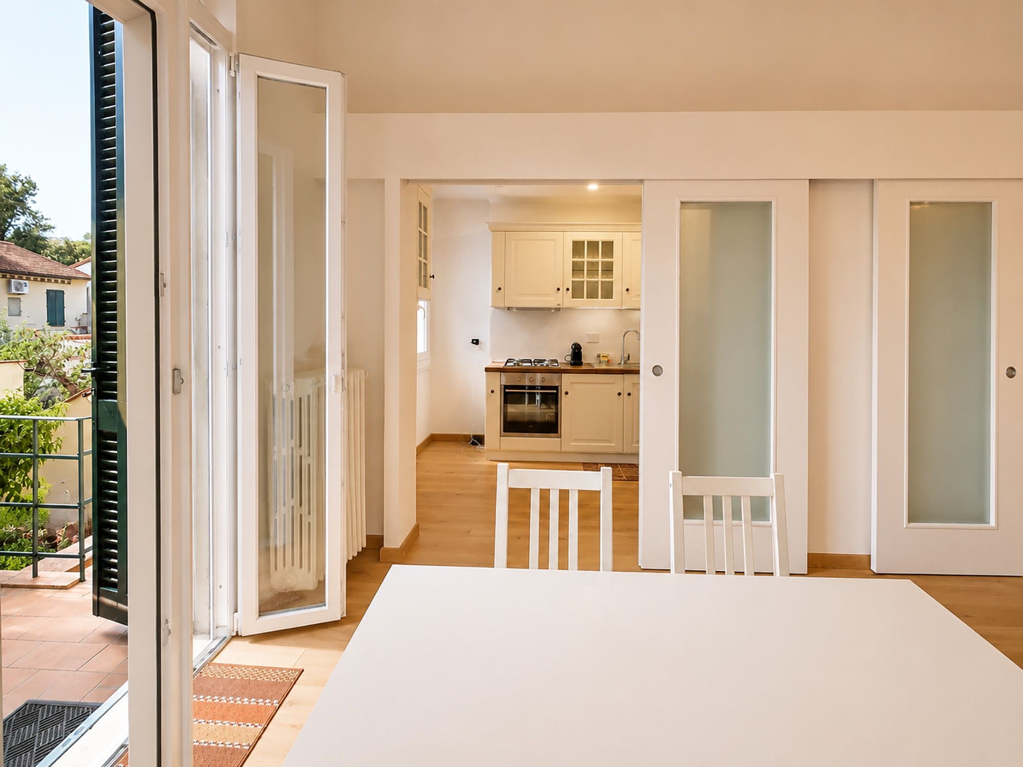 A modern kitchen with white cabinets, a dining table with chairs, and a sliding glass door leading to an outdoor area.