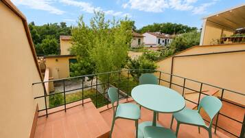 Un balcón con una mesa y sillas, vista a casas vecinas y un árbol.