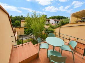 Een balkon met een tafel en stoelen, uitzicht op omliggende huizen en een boom.