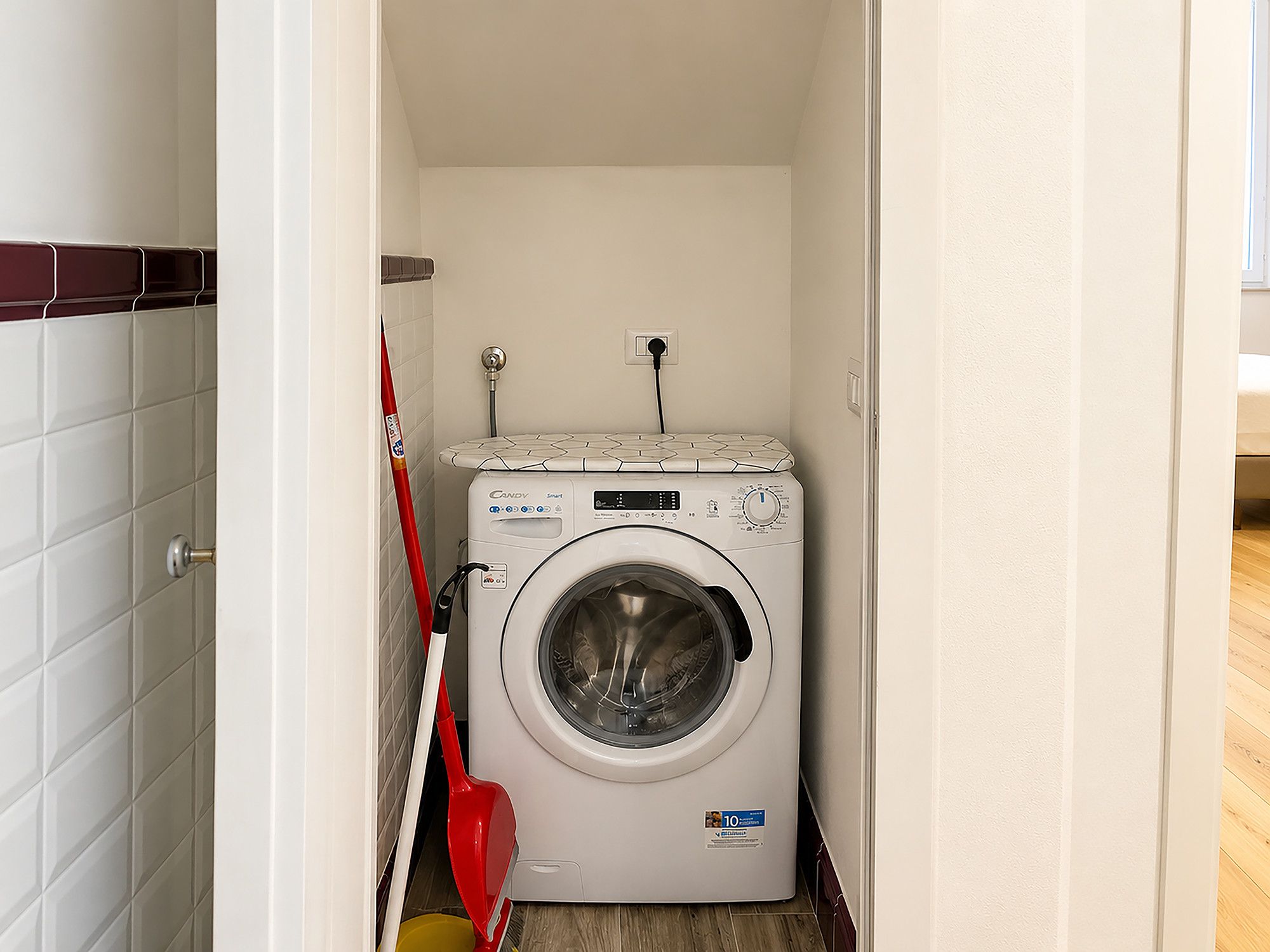 A compact laundry room with a front-loading washing machine, a red mop, and a yellow bucket.