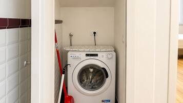 A compact laundry room with a front-loading washing machine, a red mop, and a yellow bucket.