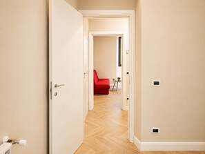 Ein Flur mit einem roten Sofa, einem kleinen Tisch mit einer Pflanze und einer Tür zu einem anderen Raum.