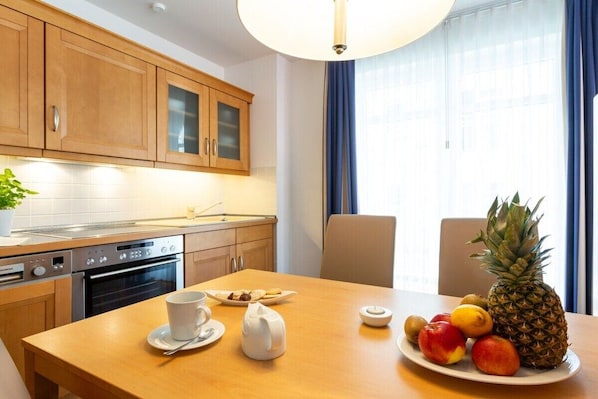 Ein Hotelzimmer mit Holztisch, gedeckt für das Frühstück, inklusive Obst und Gebäck, sowie einer modernen Küche mit Geräten.