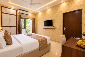 A hotel room with a bed, a TV, a desk with fruit, and a balcony.