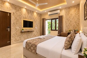 A hotel room with a bed, a TV, a window with curtains, a ceiling fan, and an air conditioning unit.