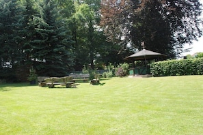 Ein gepflegter Rasen mit einem Gazebo, Picknicktischen und verschiedenen Bäumen.