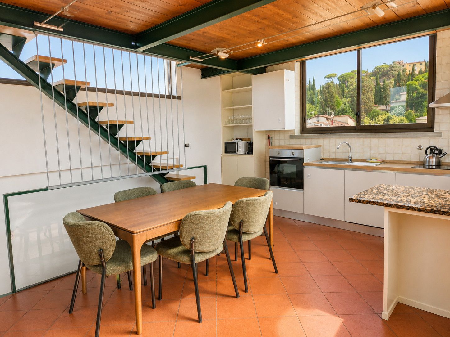 Cocina moderna con comedor, una escalera y vistas al exterior.