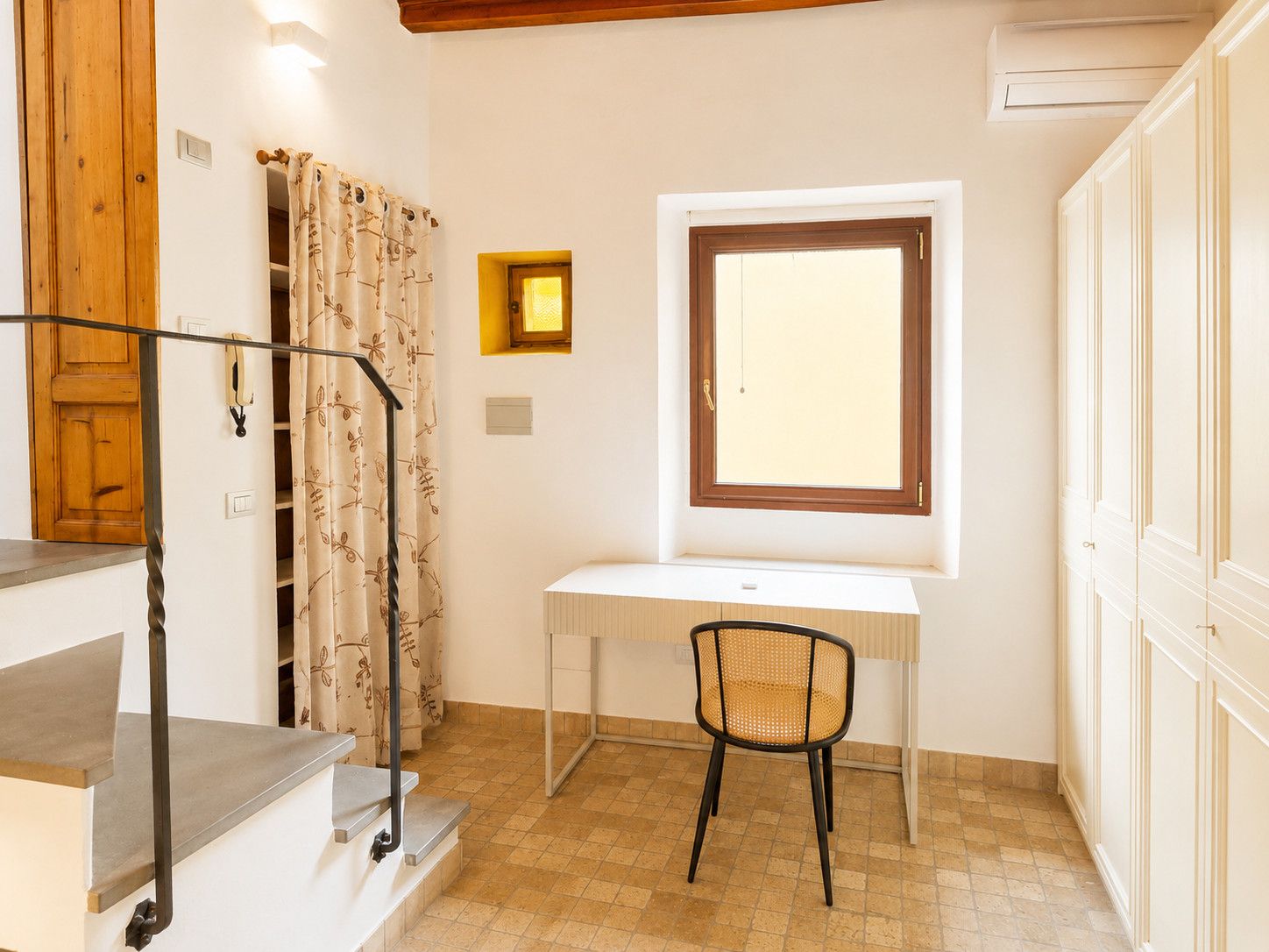Una habitación pequeña y bien iluminada con un escritorio, una silla y un ventanal.