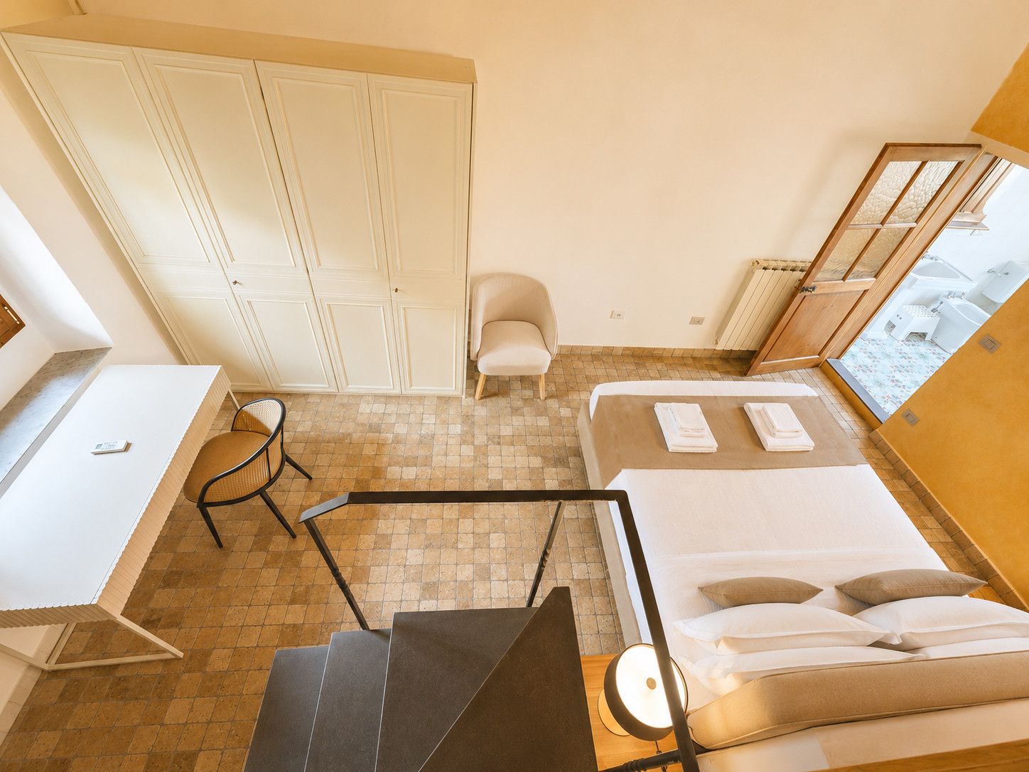 A hotel room with a bed, a desk, a chair, and a wardrobe.