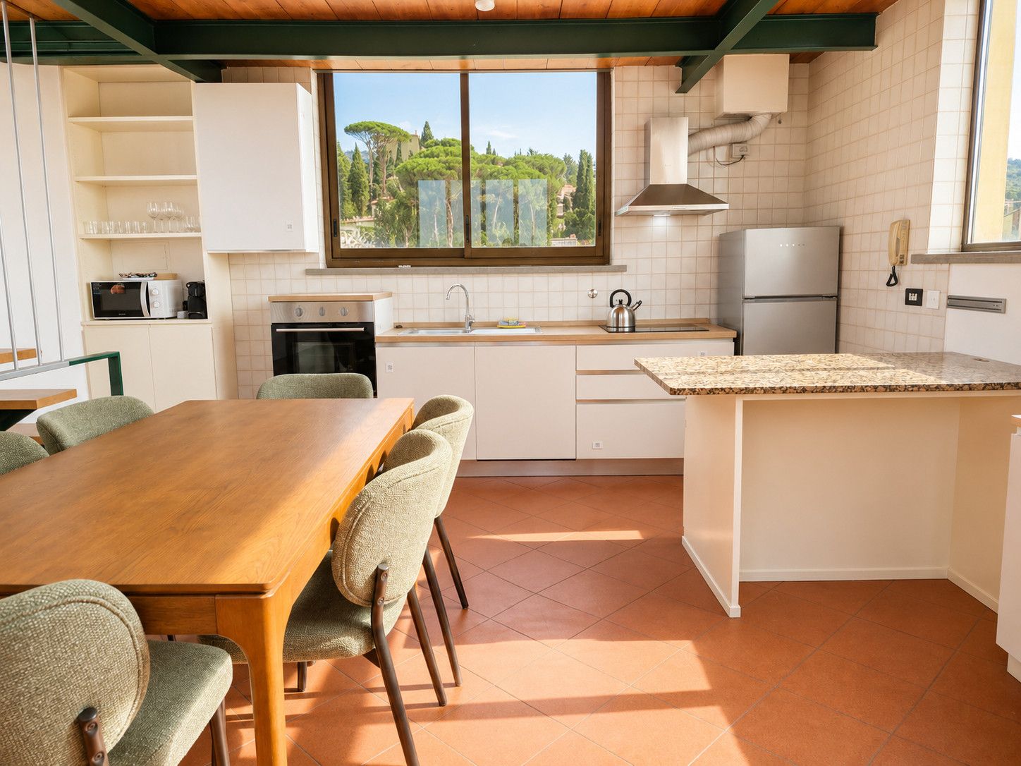 Cocina moderna con comedor, que cuenta con un amplio ventanal, muebles blancos y una mesa de comedor de madera.