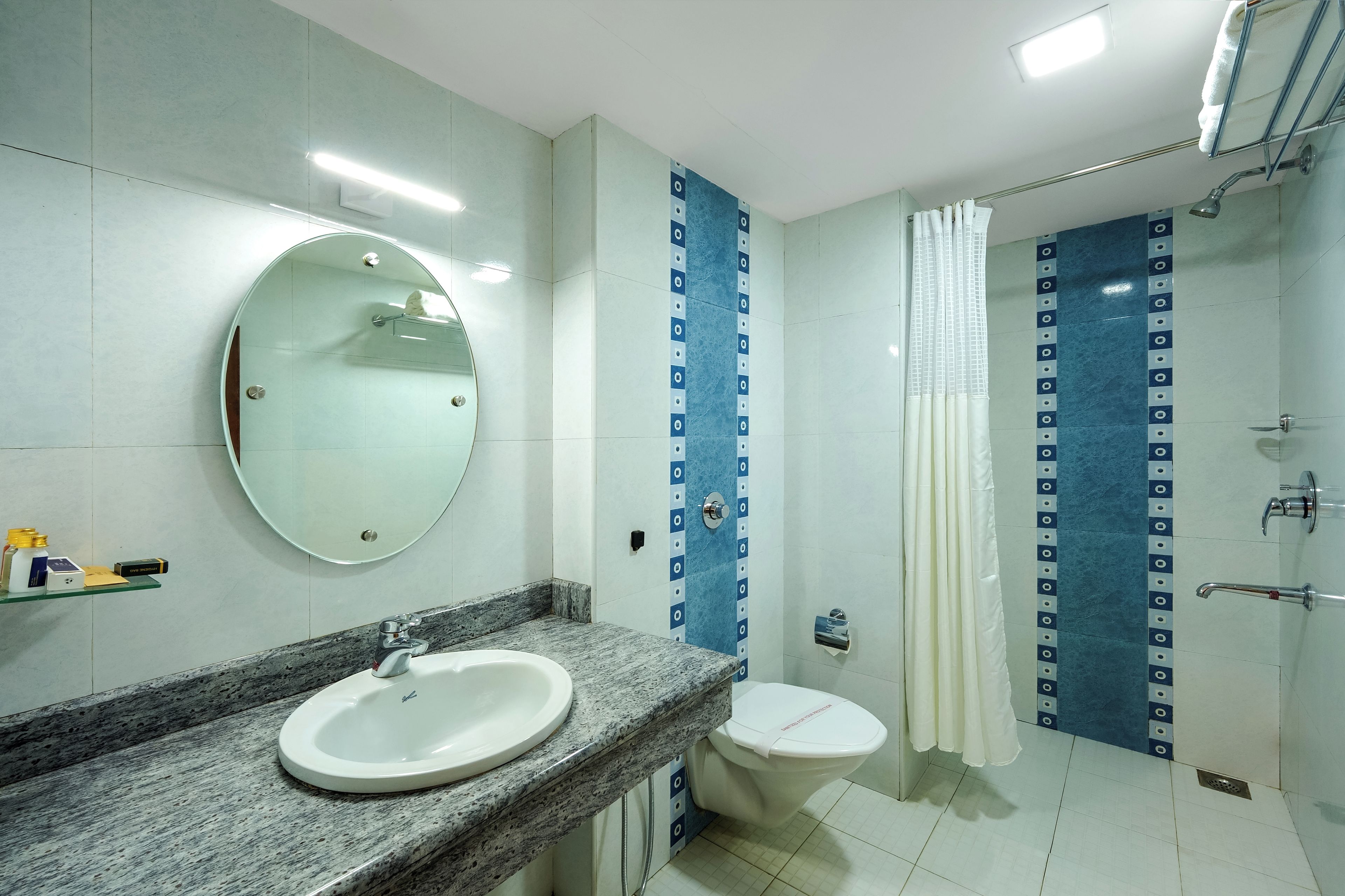 Un baño con un espejo redondo, un lavabo, un inodoro y una zona de ducha.