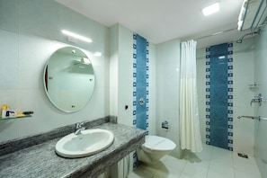 Un baño con un espejo redondo, un lavabo, un inodoro y una zona de ducha.