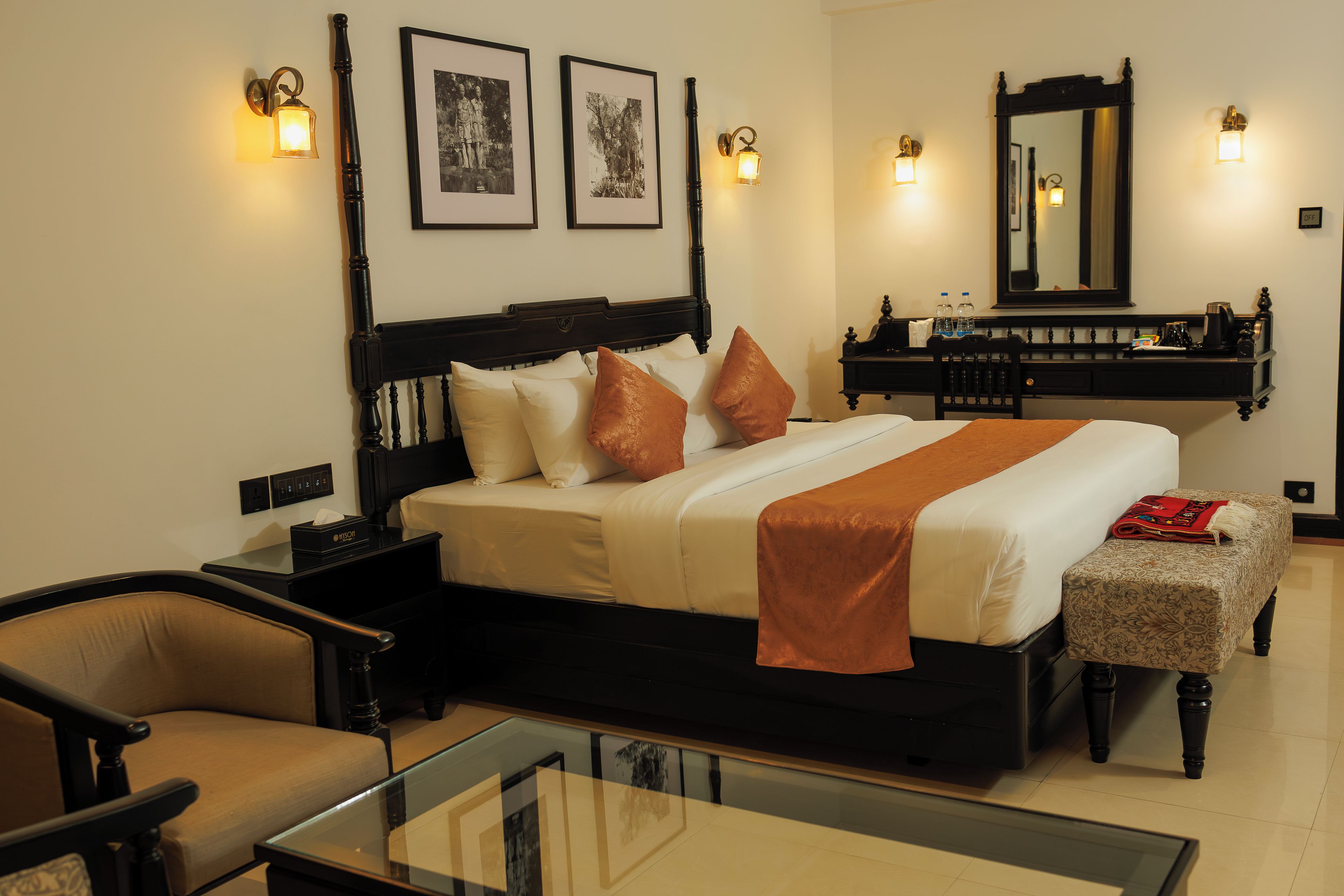 Una habitación de hotel con cama, mesitas de noche, una silla, escritorio, espejo e iluminación en la pared.