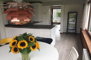 A modern kitchen with a central island, a dining table with a vase of sunflowers, and a view into the adjacent living area. - Holiday home in Maasholm with swimming pool (Maasholm)