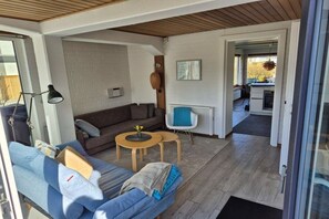A compact living space with a sofa, a small table, and a chair. There is a kitchen area visible through an open doorway. - Holiday home in Maasholm with swimming pool (Maasholm)