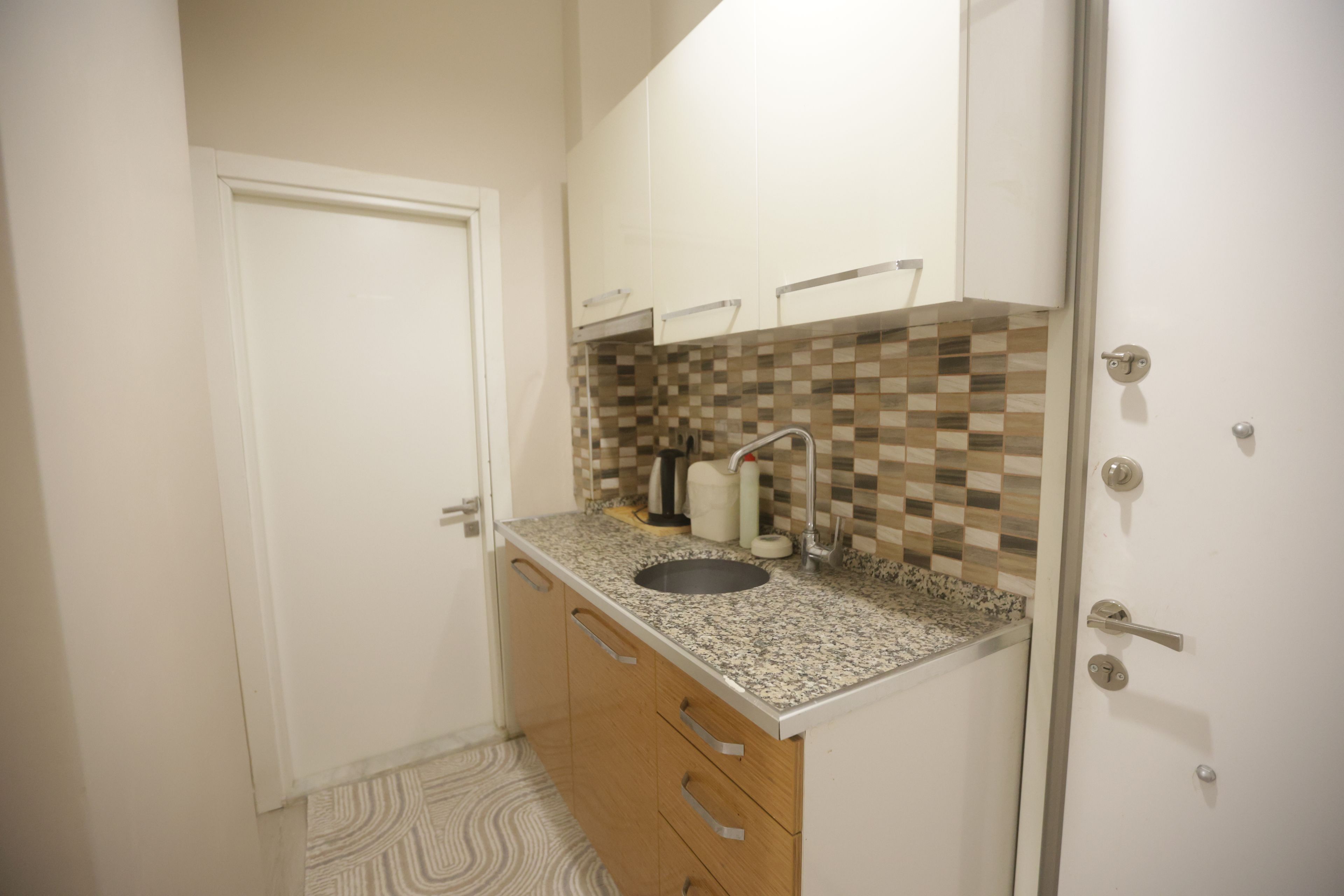 A small kitchen with a sink, cabinets, and a patterned floor.