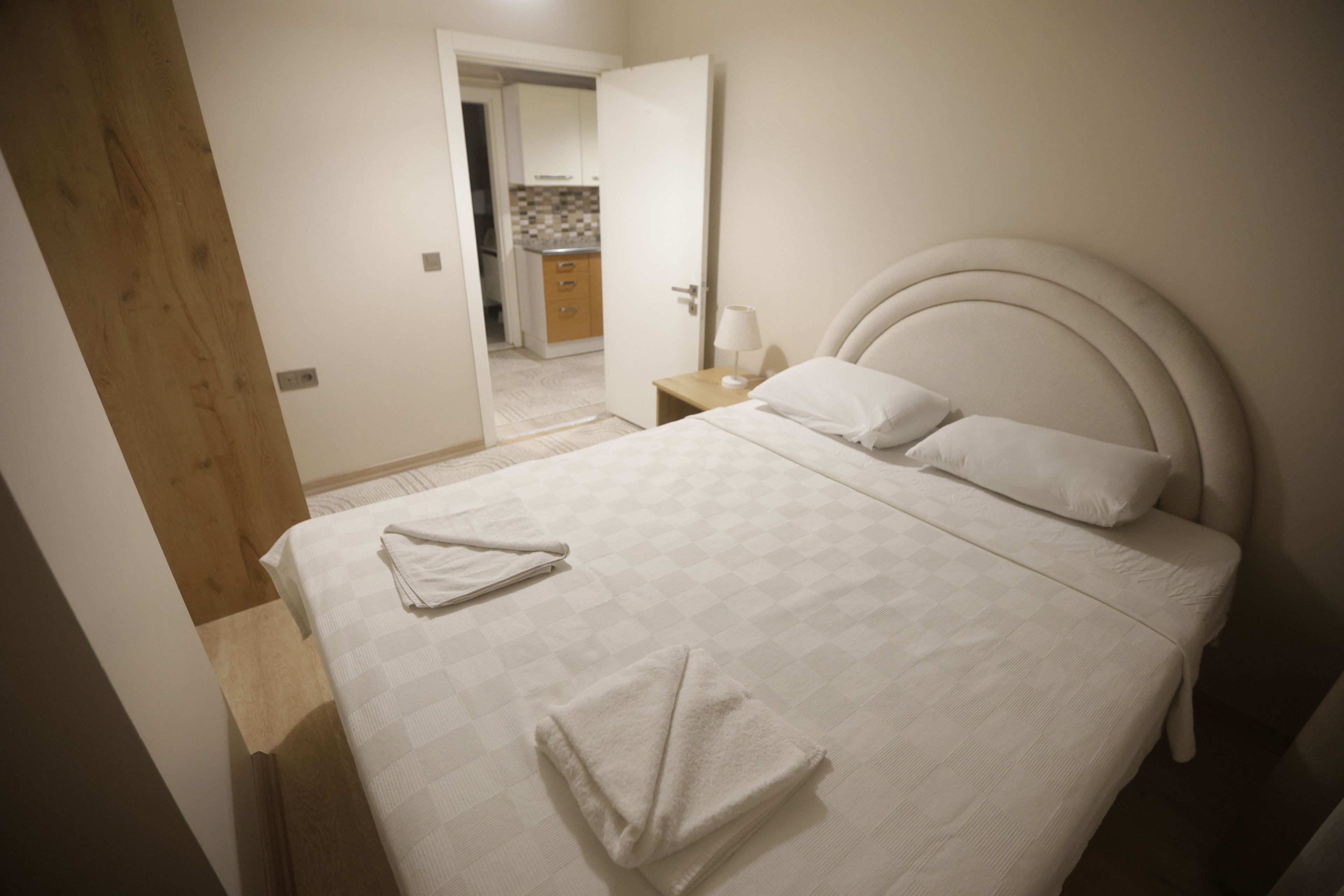 A neatly made bed with a headboard, a bedside table with a lamp, and a bathroom visible through an open door.
