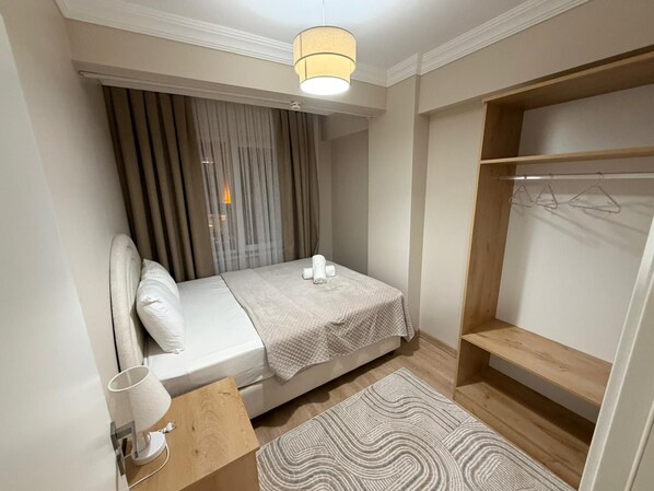 Un dormitorio compacto con cama, mesita de noche, lámpara y armario con barra para colgar.