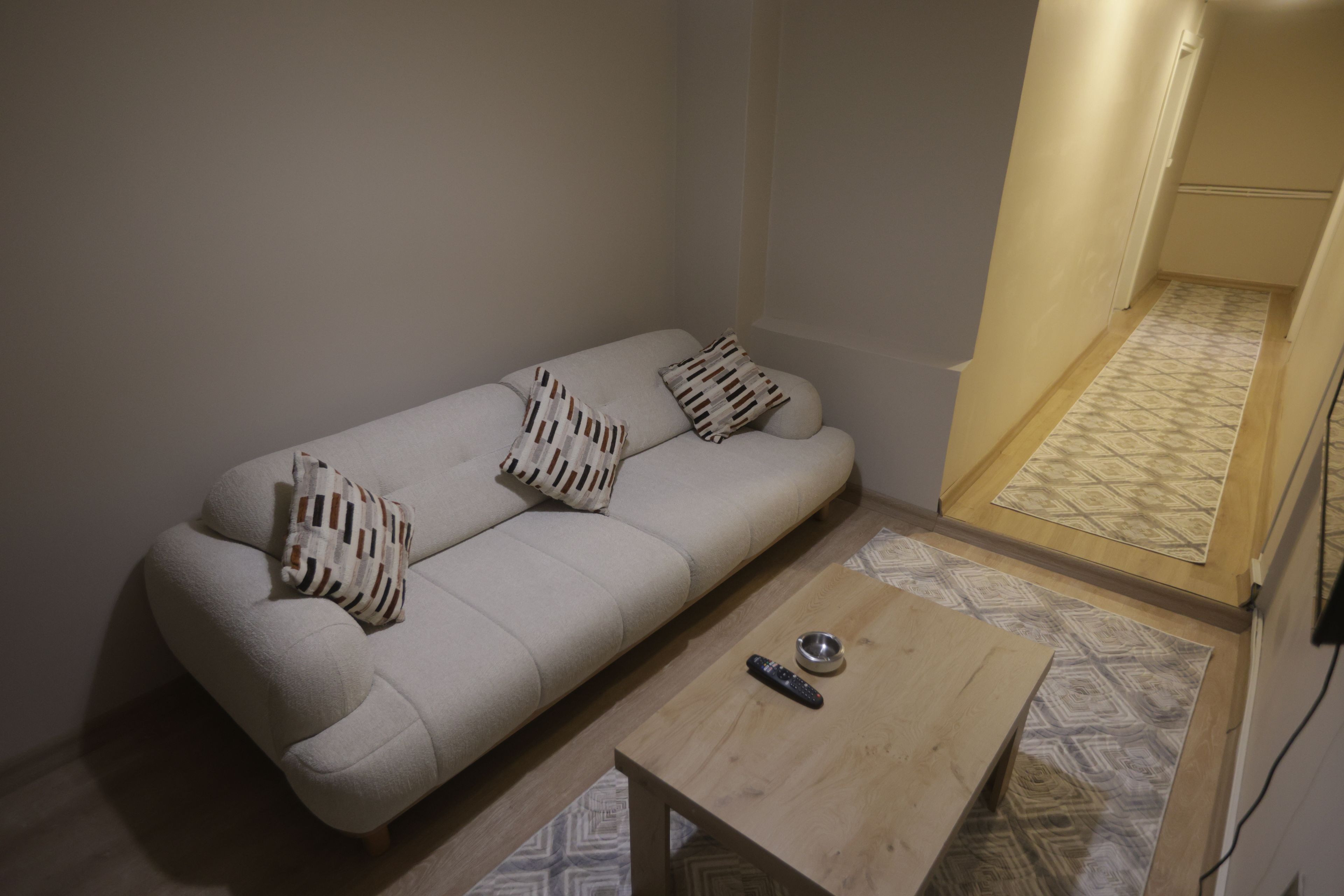 Ein Zimmer mit einer Couch, Kissen, einer Fernbedienung und einem Holztisch.