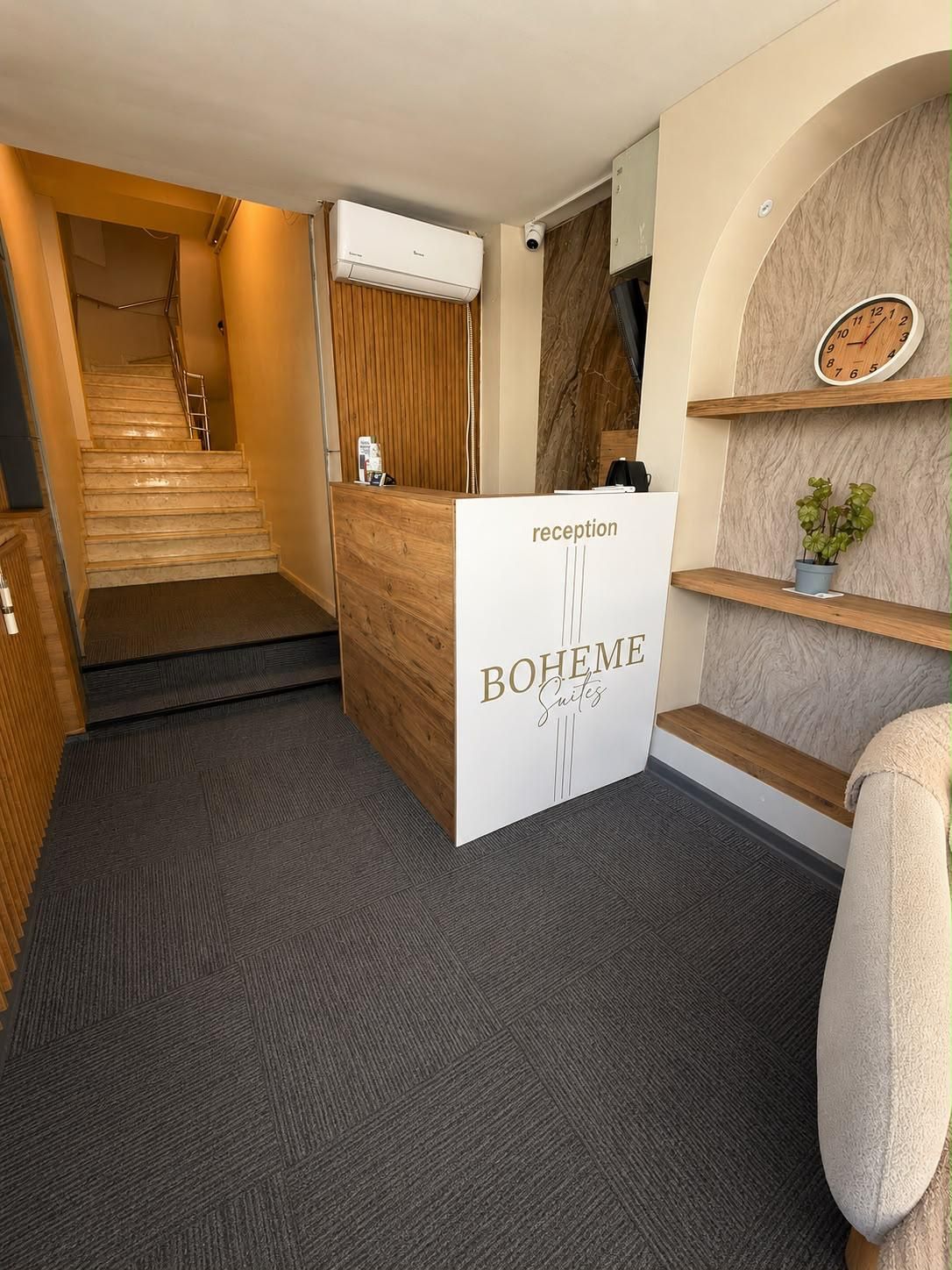 En receptionsdisk med en skylt där det står ”BOHEME Suites” och en klocka på väggen.