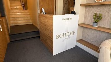 En receptionsdisk med en skylt där det står ”BOHEME Suites” och en klocka på väggen.
