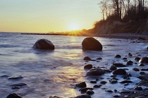 A beach with rocks and a sunset in the background. - Beach house type "sailor" (Schashagen OT Bliesdorf-Strand)