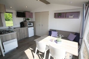 A compact kitchen with a dining area, a TV mounted above the counter, and a small window. - Beach house type "sailor" (Schashagen OT Bliesdorf-Strand)