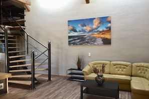 A staircase with a metal railing, a yellow leather sofa, a black coffee table, and a painting of a coastal landscape on the wall. - Holiday apartment with 1 bedroom (Bastorf (OT Kägsdorf))