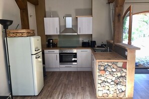 Een compacte keuken met een koelkast, oven en een inbouwfornuis. Er is een houten aanrecht en een wand van steen.