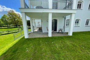 A two-story building with a covered patio area, a balcony, and a view of a well-maintained lawn. - Strandpalais Kühlungsborn "Starboard" (Kühlungsborn)