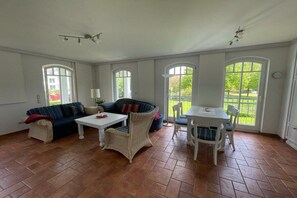 Ein geräumiges Zimmer mit großem Fenster, einer Couch, einem Tisch und einem Sessel.