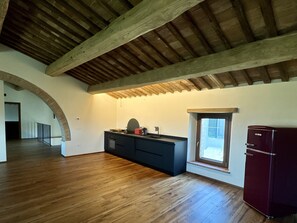 A spacious kitchen with wooden beams, a dark countertop, and a red refrigerator. - Camigliano Wine Estate - Oliviera (Camigliano)