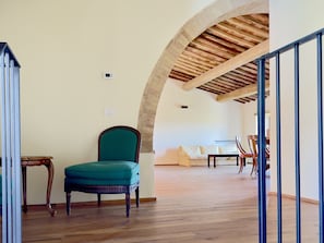 Habitació amb sòl de fusta, una cadira color turquesa, un tauler de fusta i un sofà blanc.