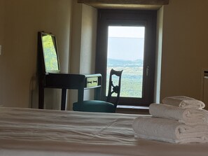 A hotel room with a bed, a desk with a mirror, a chair, and a view through a window. - Camigliano Wine Estate - Oliviera (Camigliano)