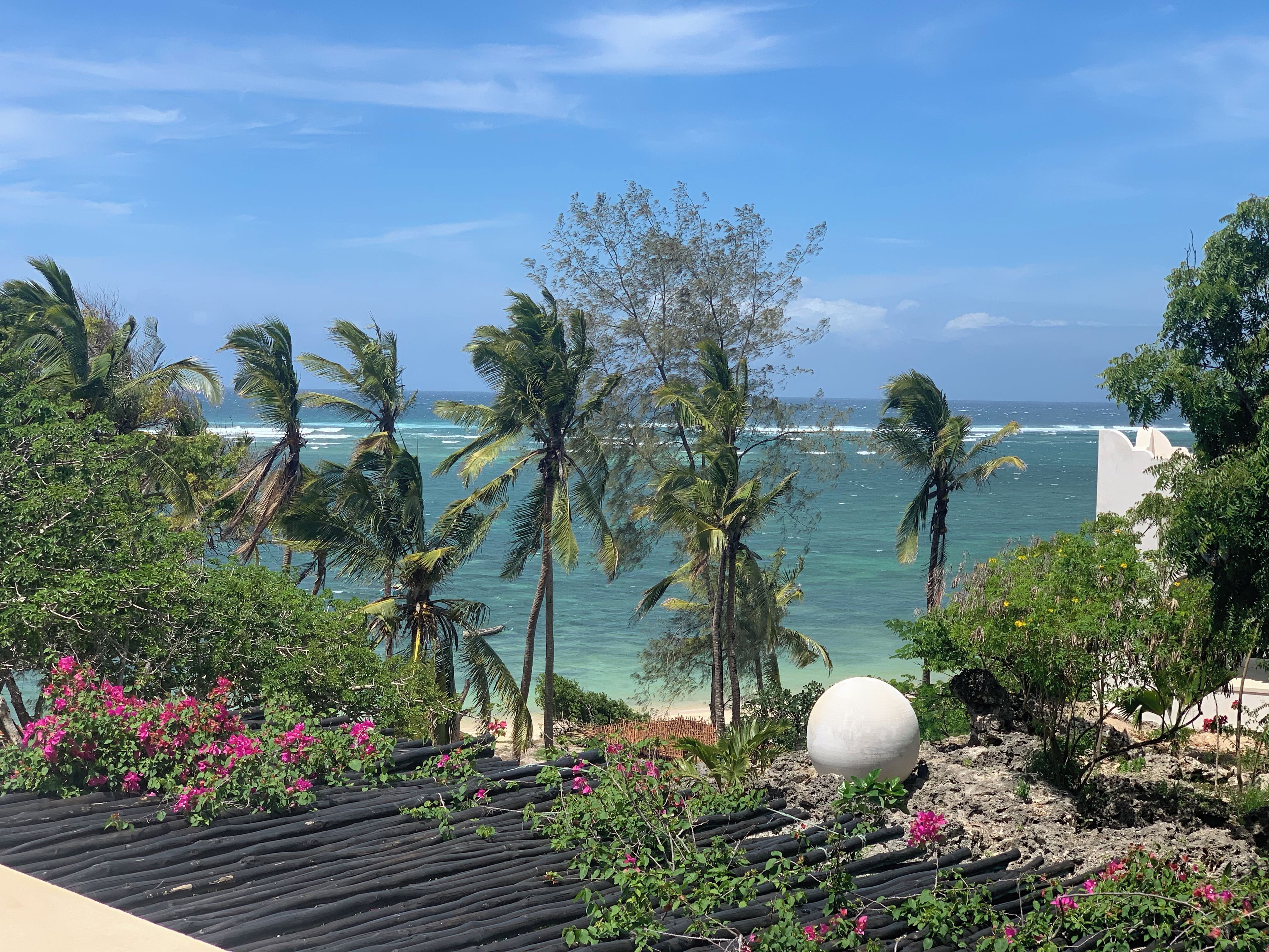 A coastal view with palm trees, a beach, and a large spherical structure.