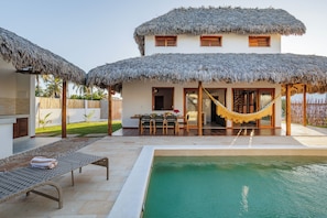 A poolside area with a thatched-roof structure, a dining table, and a hammock. - Casa Ariah Luxury Villas (Cruz)