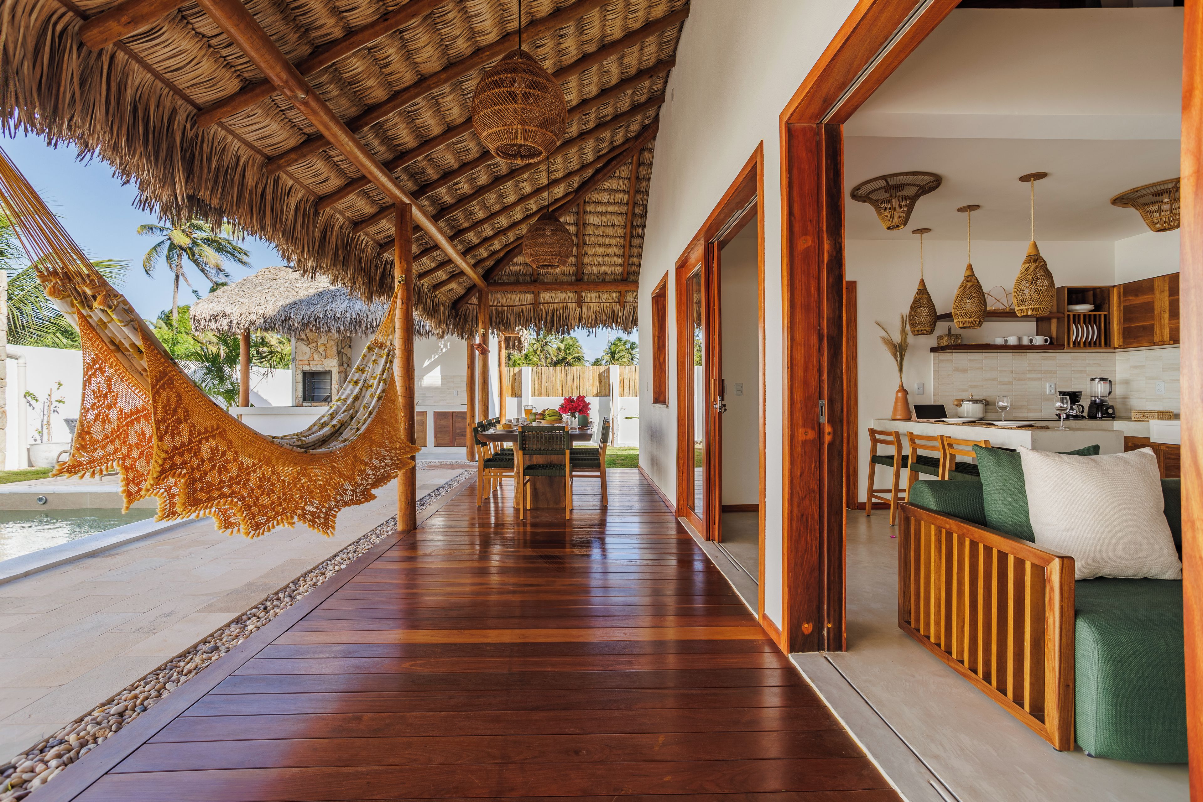 A wooden deck with a hammock, a dining area, and a kitchen with wooden cabinets and hanging lights.