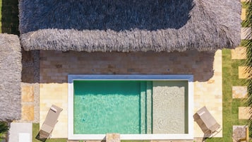 Una piscina rectangular con agua cristalina, rodeada por un muro de piedra y una estructura de techo de paja.