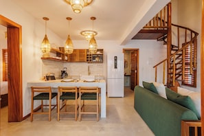 A modern kitchen with a central island, wooden chairs, and a green sofa in a living area. - Casa Ariah Luxury Villas (Cruz)