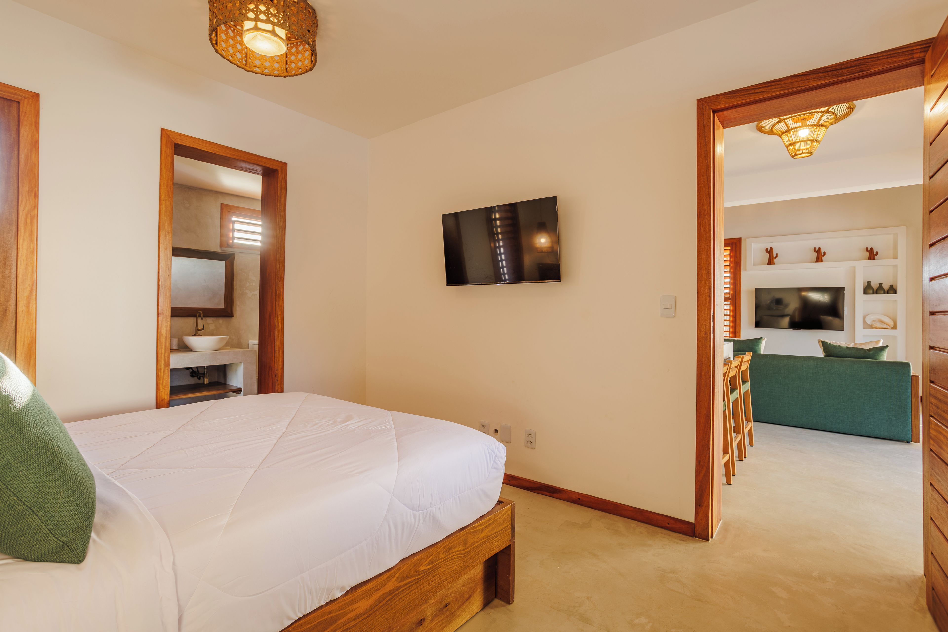Un dormitorio con cama, televisor montado en la pared y un baño visible a través de una puerta abierta.