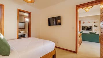 Un dormitorio con cama, televisor montado en la pared y un baño visible a través de una puerta abierta.