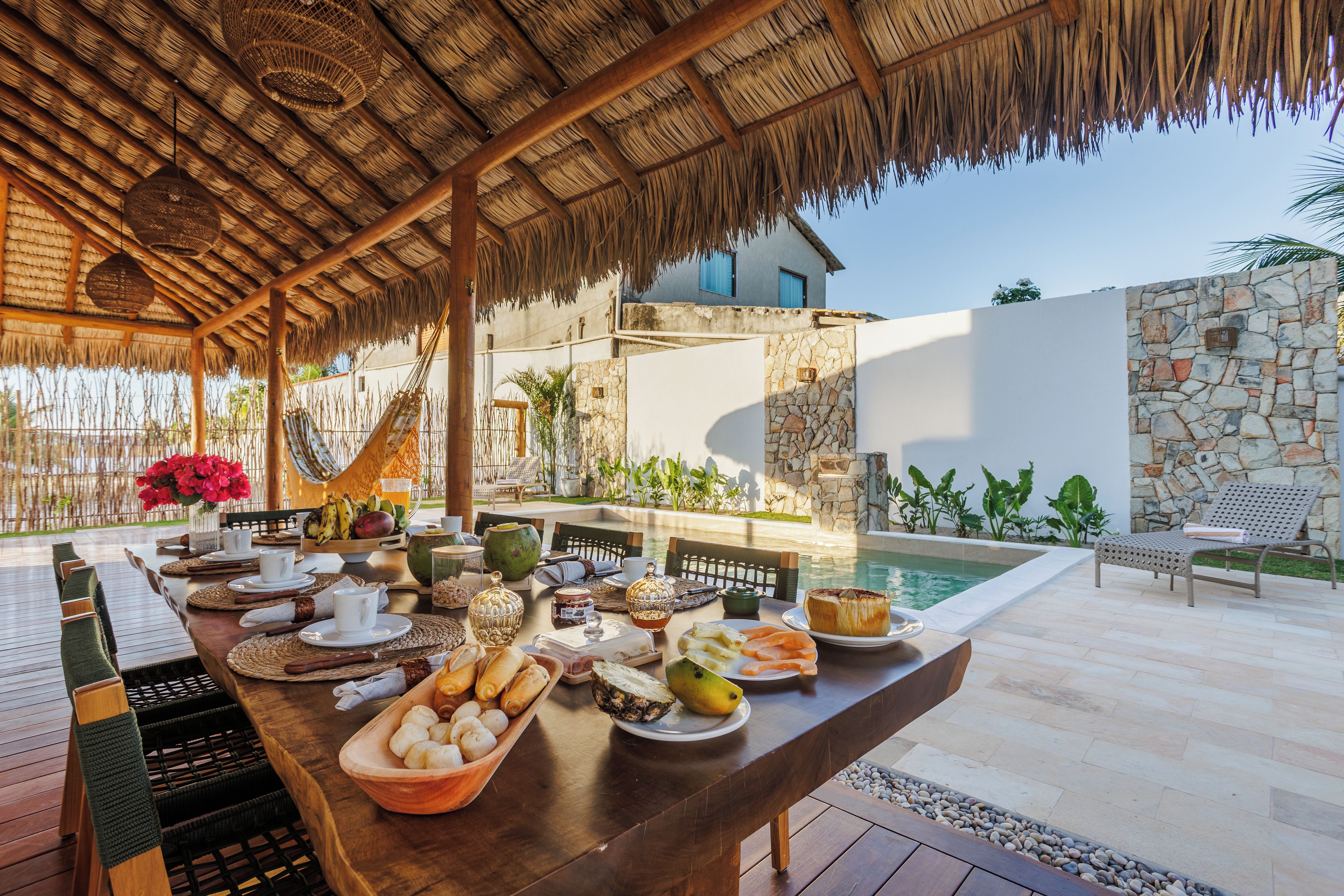 An outdoor dining area with a pool view, wooden furniture, and a variety of food and drink items.
