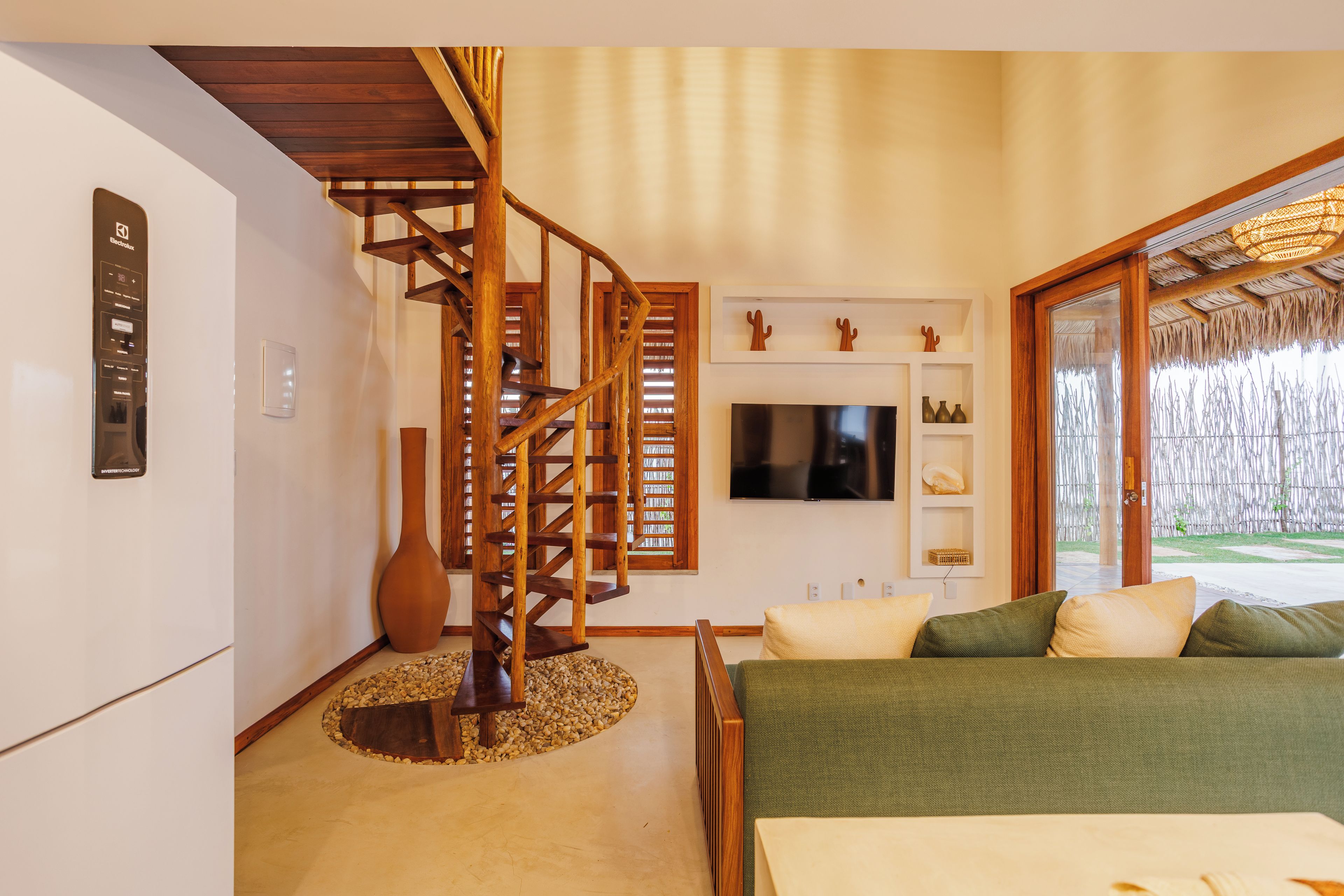 A modern interior with a wooden spiral staircase, a flat-screen TV, and a bed with multiple pillows.