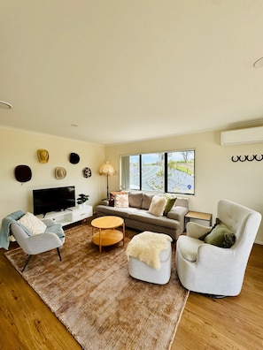 A modern living room with a sofa, armchairs, a coffee table, and a television. - Escape the city and slow down at 'The Ranch', 1.5 hours North of Auckland. (Paparoa)