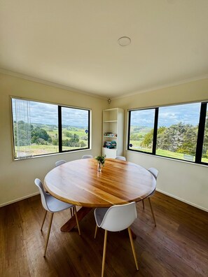 A round wooden table with white chairs in a room with large windows. - Escape the city and slow down at 'The Ranch', 1.5 hours North of Auckland. (Paparoa)