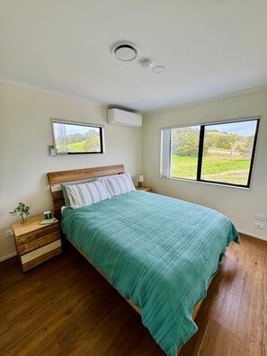 A bedroom with a bed, bedside tables, an air conditioning unit, and windows with a view of greenery. - Escape the city and slow down at 'The Ranch', 1.5 hours North of Auckland. (Paparoa)